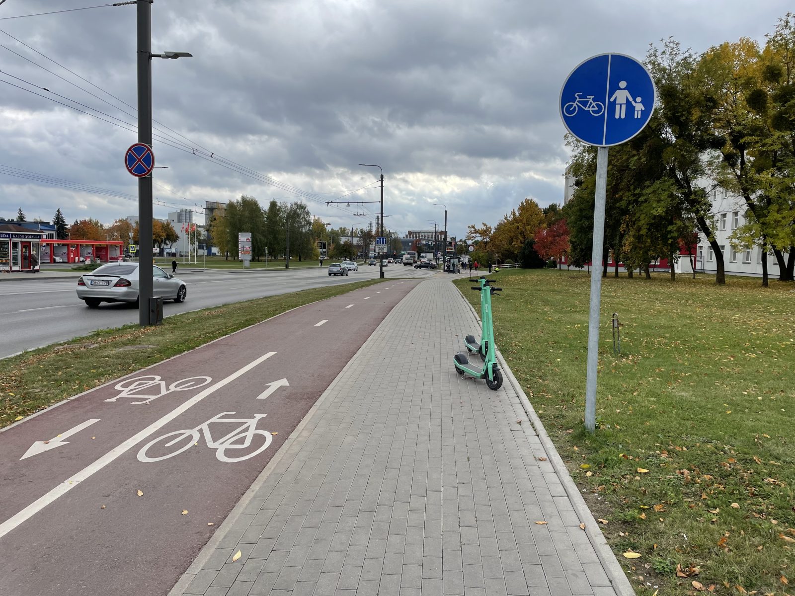 Pėsčiųjų ir dviračių takas palei gatvę Kaune rudenį, ant šaligatvio stovi du paspirtukai