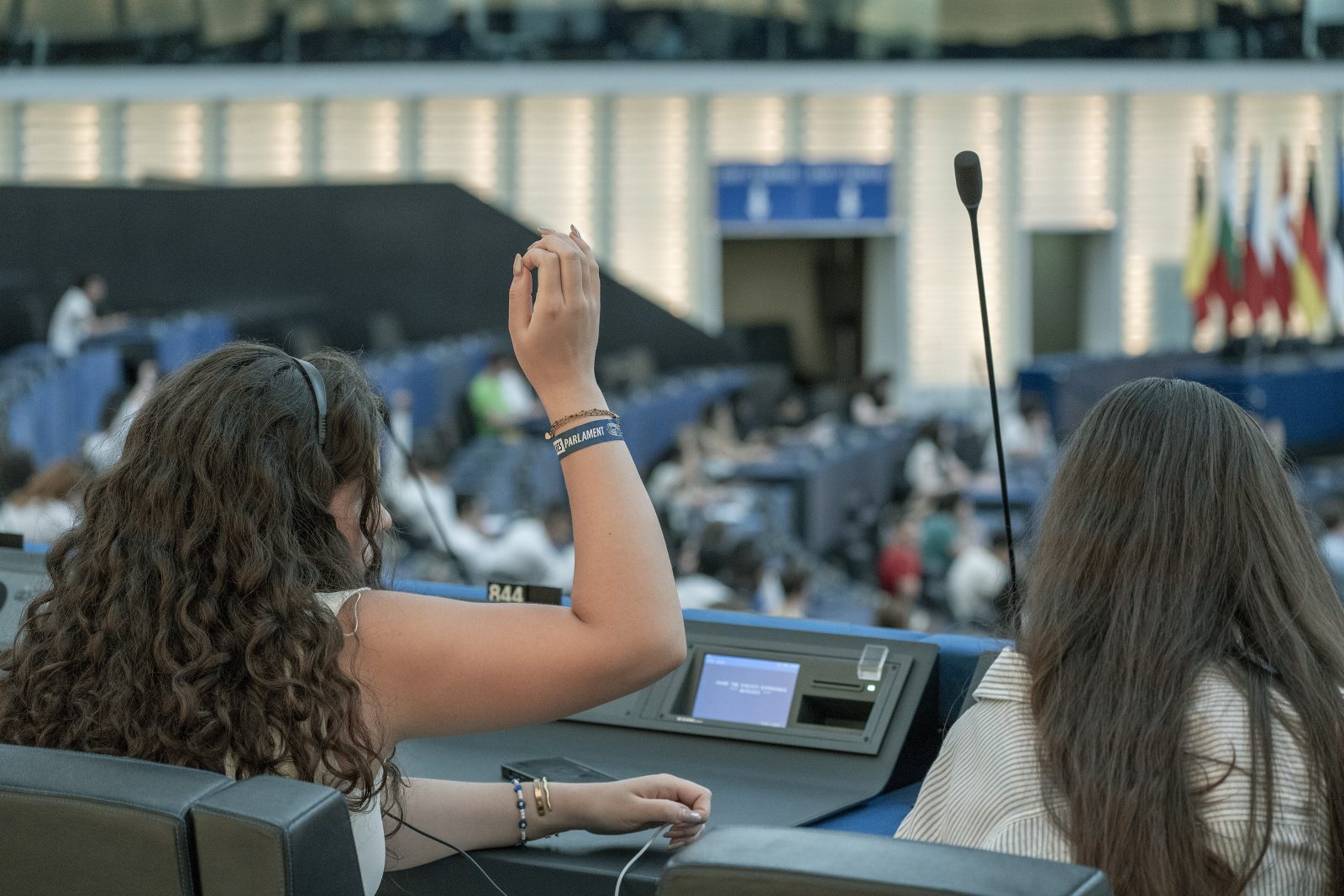 Jaunos merginos Europos Parlamento posėdžių salėje kelia rankas norėdamos pasisakyti