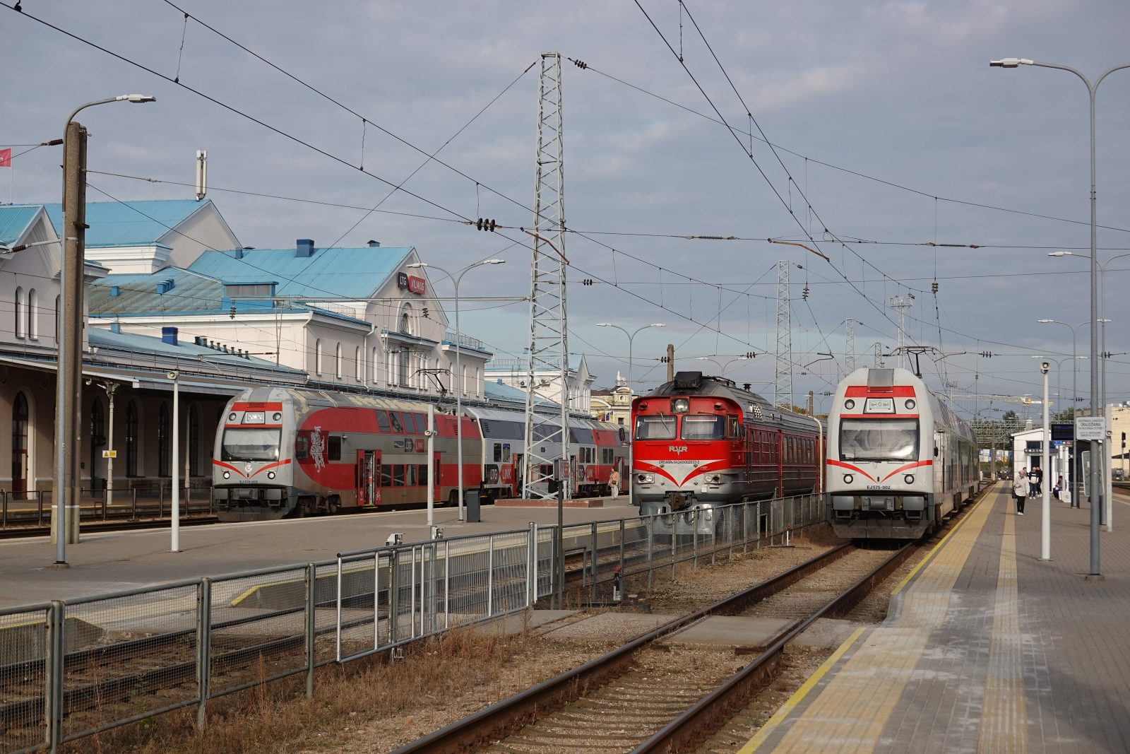 Vilniaus geležinkelio stotis: prie peronų stovi du dviaukščiai elektriniai traukiniai ir raudonas dyzelinis traukinys